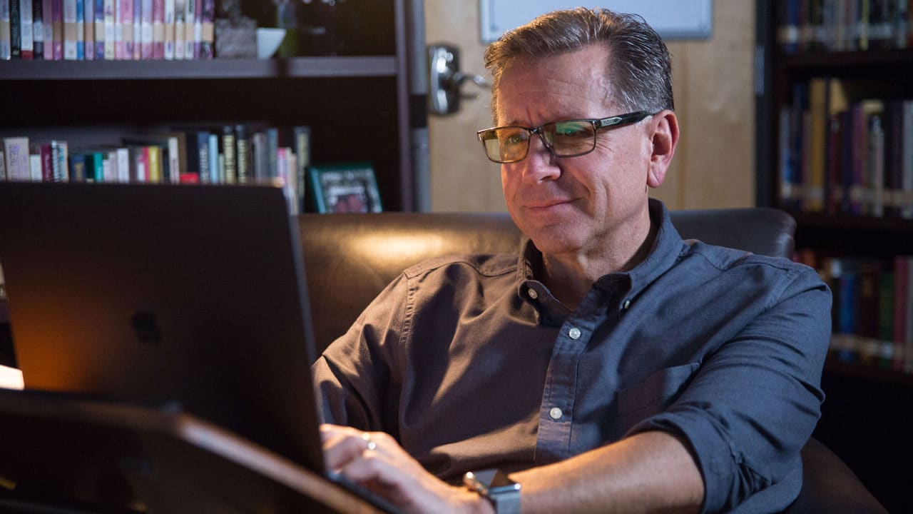 Pastor Mike Fabarez working in his library on a laptop